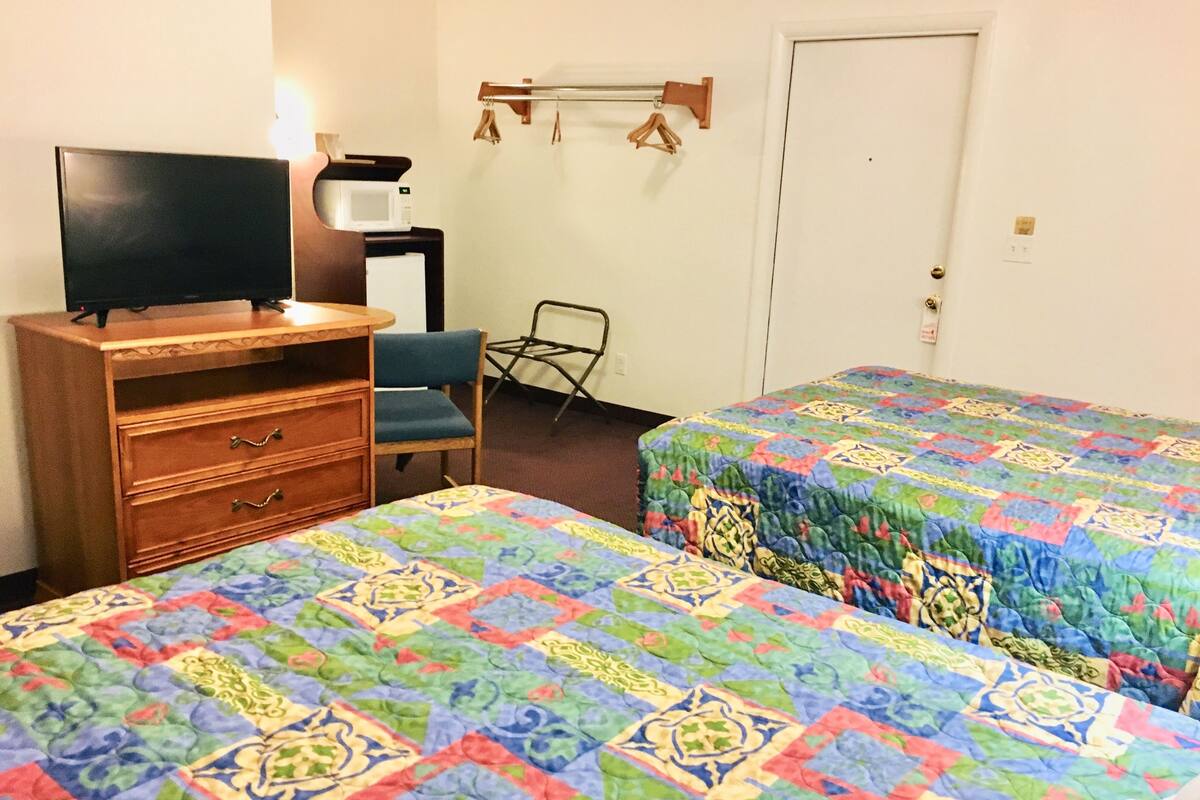 A hotel room with two beds, a wooden dresser, a television, and a chair.