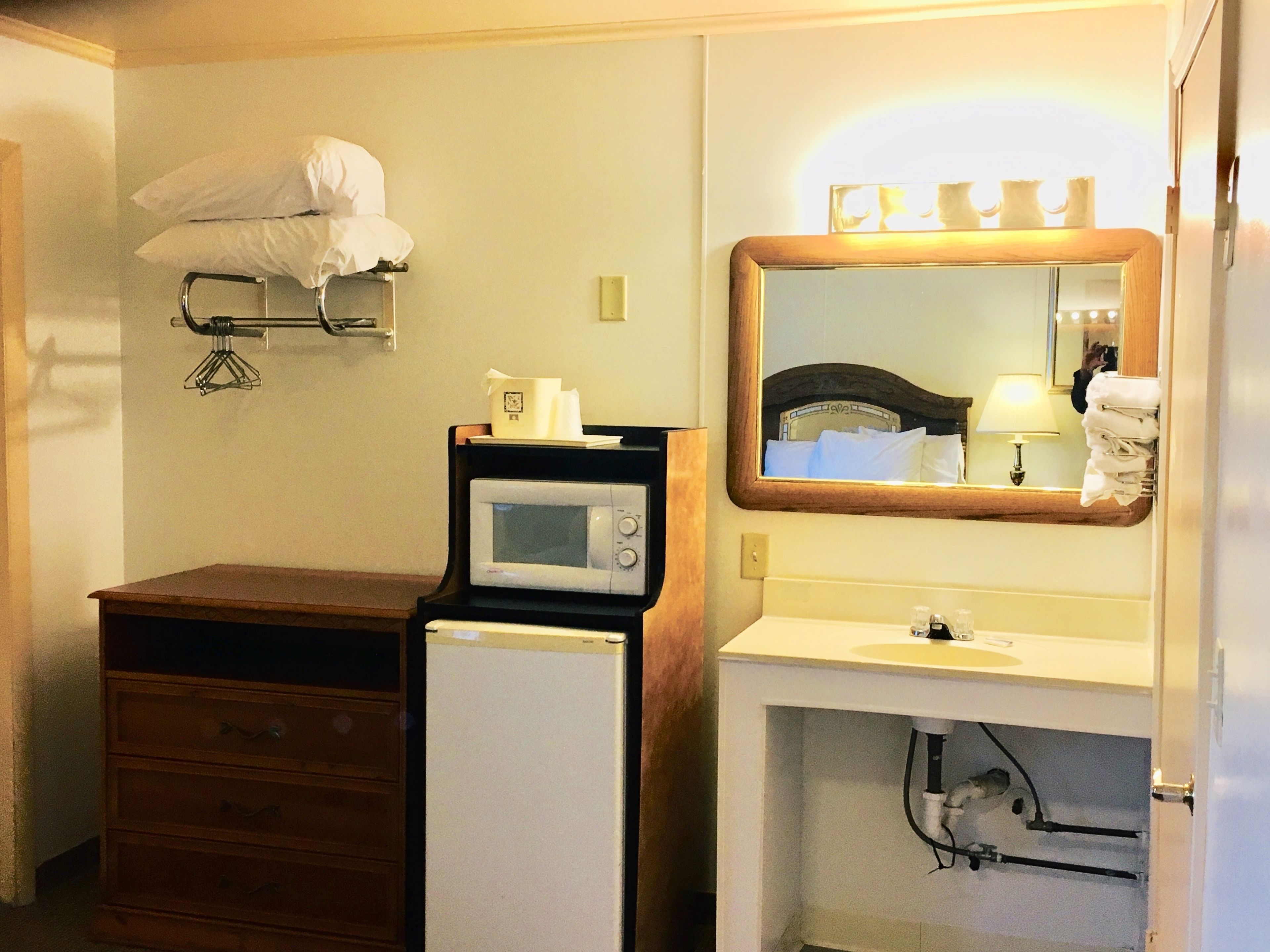 A compact hotel bathroom with a microwave, a sink, and a mirror.