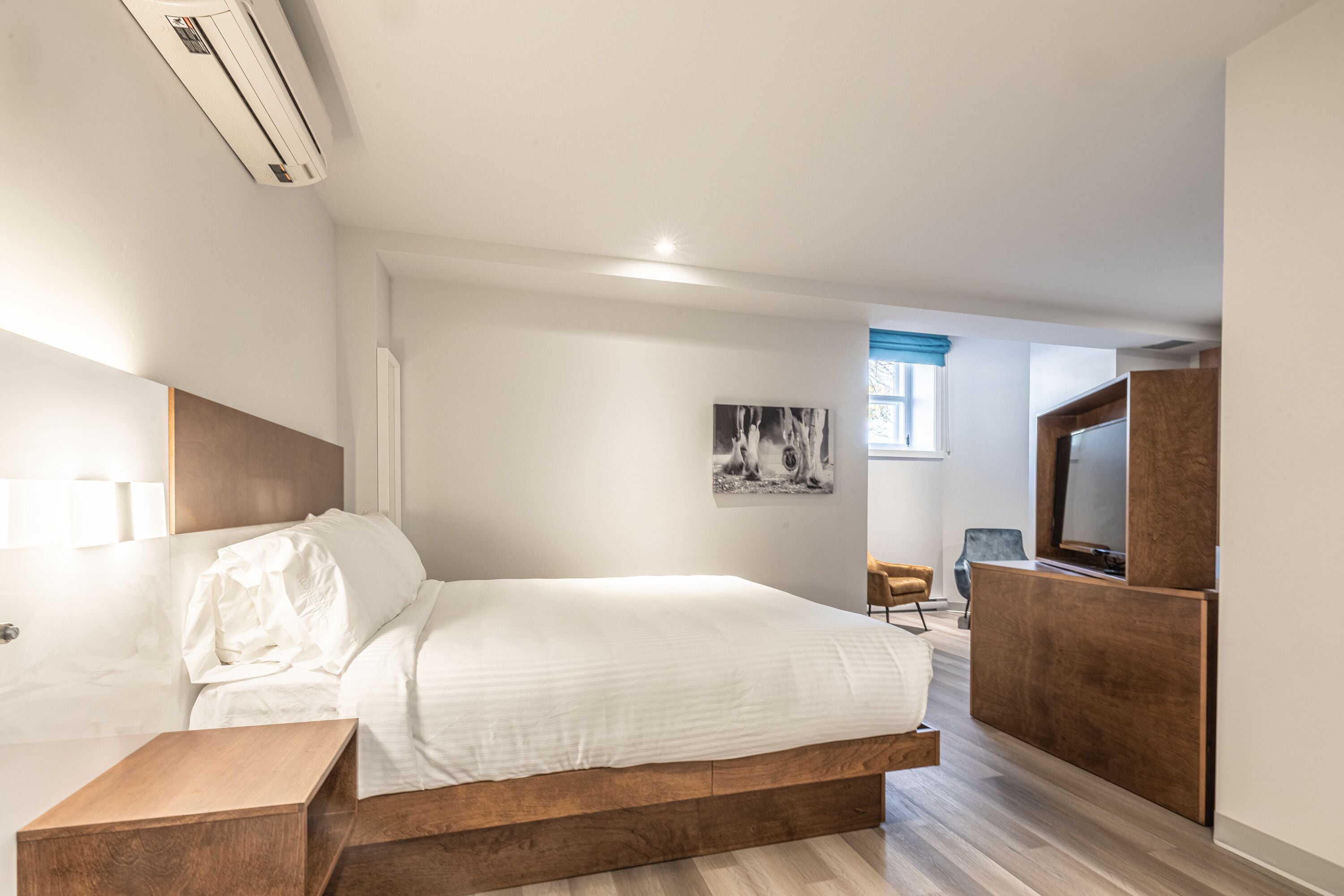 A modern hotel room with a large bed, a wooden nightstand, a TV, and a painting on the wall.