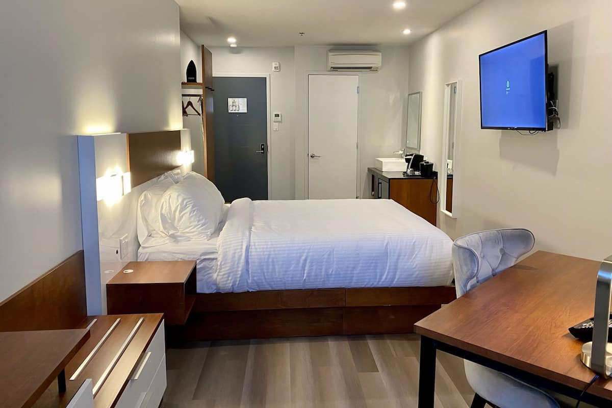 Ein Hotelzimmer mit Bett, Nachttisch, Schreibtisch, Stuhl, Fernseher und Spiegel.