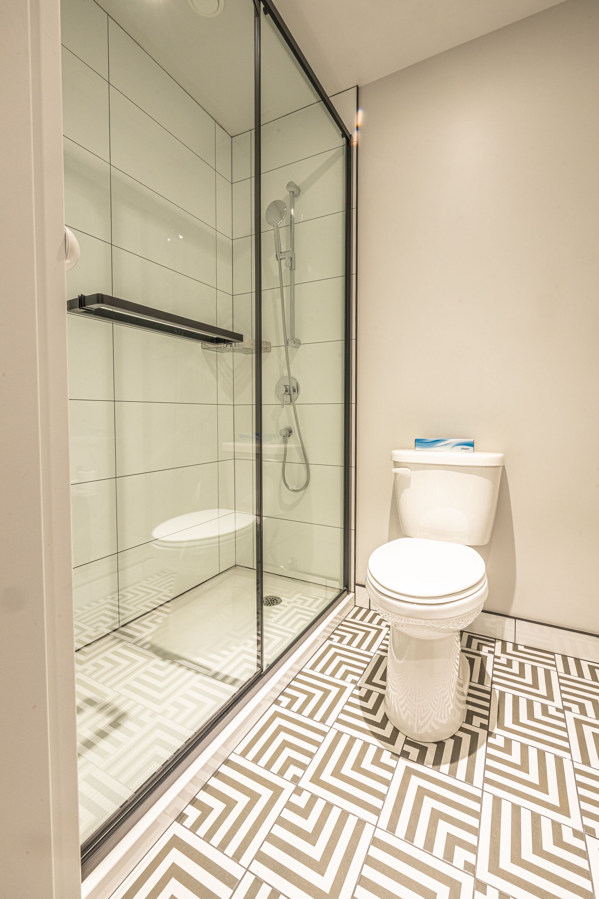 A modern bathroom with a glass-enclosed shower, a white toilet, and patterned floor tiles.