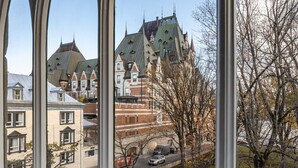 Vista a través de una ventana con arco gótico, que da a una calle con edificios y un árbol.