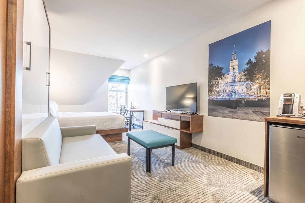 Ein Hotelzimmer mit Bett, Schreibtisch mit Fernseher, Kaffeemaschine und großem Fenster.