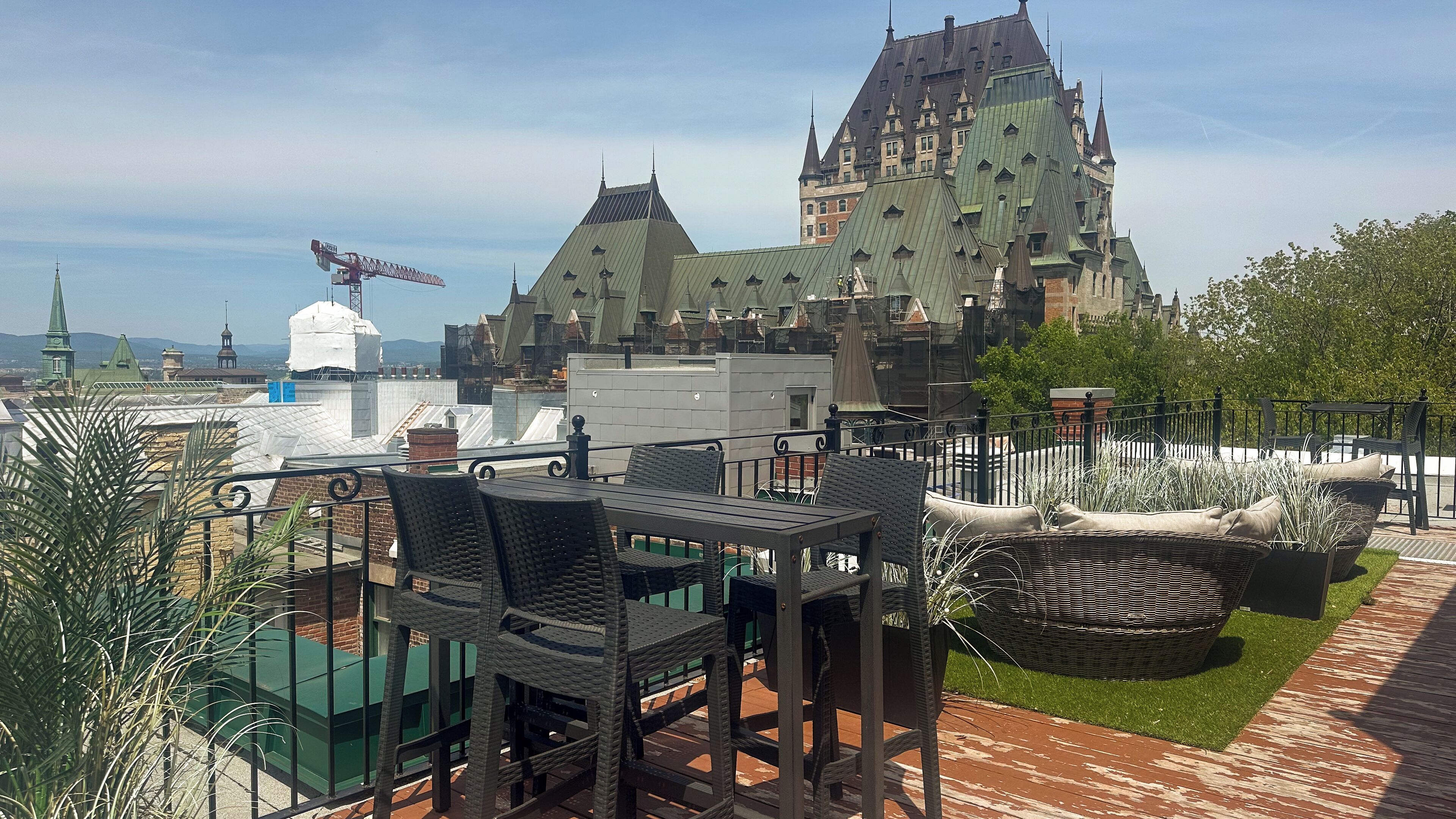 Une terrasse sur le toit, aménagée avec des meubles en osier, offrant une vue sur un bâtiment historique doté de nombreuses flèches.