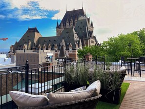 A rooftop terrace with wicker furniture, potted plants, and a view of a historic building with multiple spires. - Hôtel Manoir Vieux Québec (Québec City)