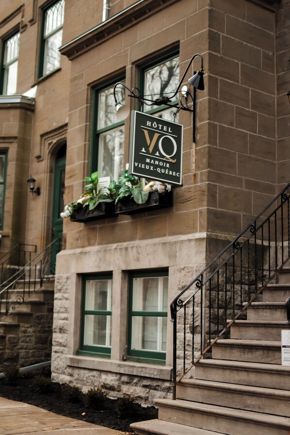 A hotel sign with "HOTEL VO MANNOIR VIX-QUÉBEC" on a stone building with green windows and a staircase. - Hôtel Manoir Vieux Québec (Québec City)