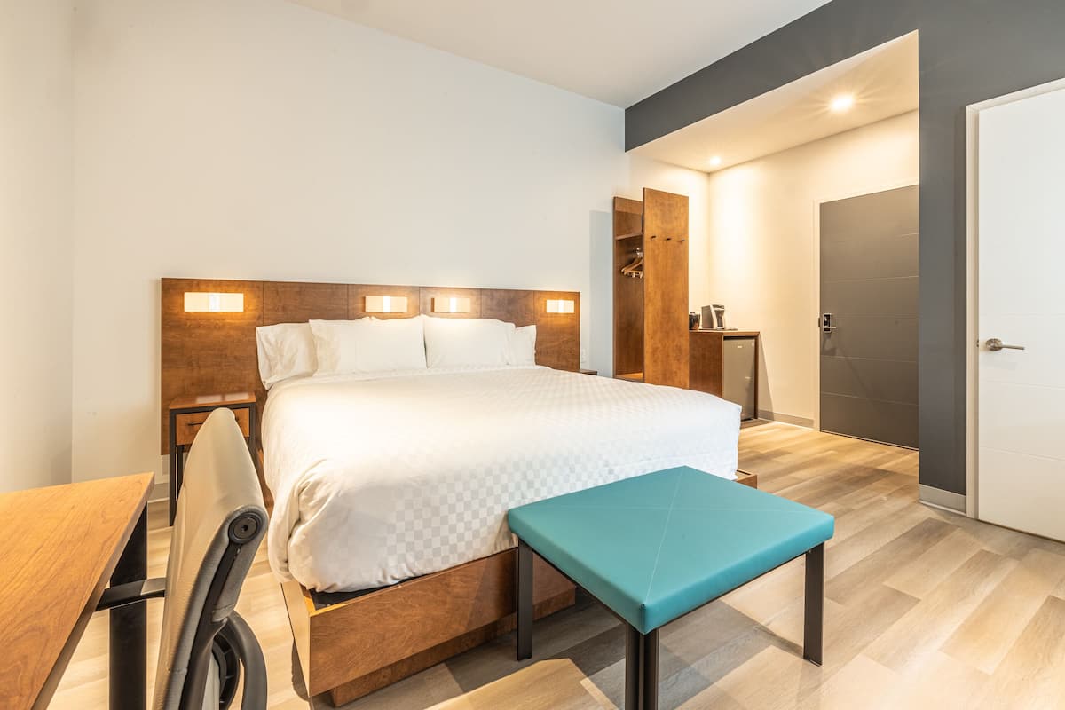 Ein modernes Hotelzimmer mit einem hölzernen Kopfteil, einem großen Bett, einem Schreibtisch und einer Bank.
