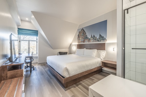 A modern bedroom with a large bed, a desk, and a chair. There is a painting on the wall and a window with a view of a building. - Hôtel Manoir Vieux Québec (Québec City)