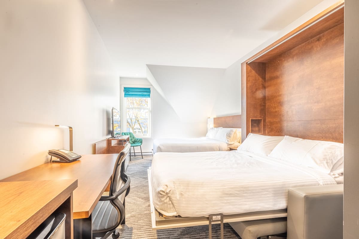 Ein Hotelzimmer mit zwei Betten, einem Schreibtisch, einem Stuhl und einem Fenster mit blauen Vorhängen.