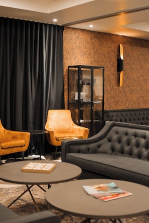 Un espacio lounge moderno con un sofá capitonado, dos sillones y una mesita redonda con revistas.