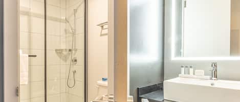 A modern bathroom with a glass-enclosed shower, a white toilet, and a sink with a mirror above it.
