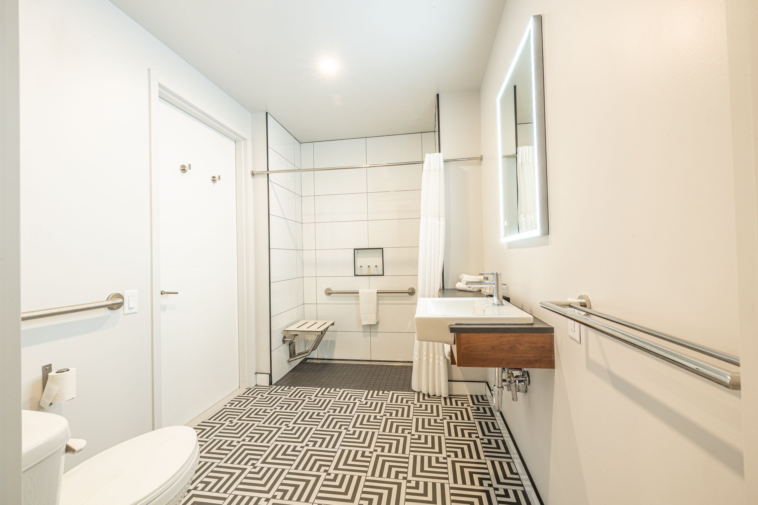 Baño con inodoro, lavamanos, espejo, toallero y piso estampado.