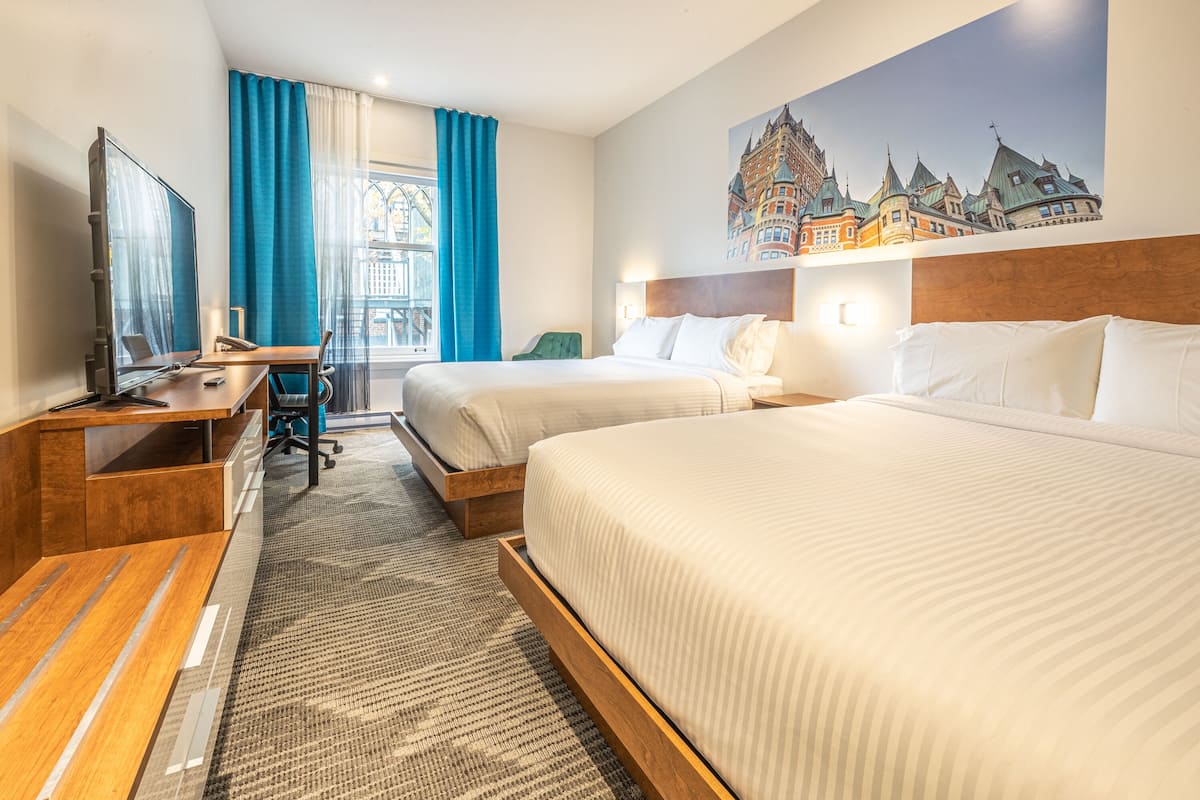 Ein Hotelzimmer mit zwei Betten, einem Schreibtisch, einem Fernseher und einem großen Fenster mit Vorhängen.