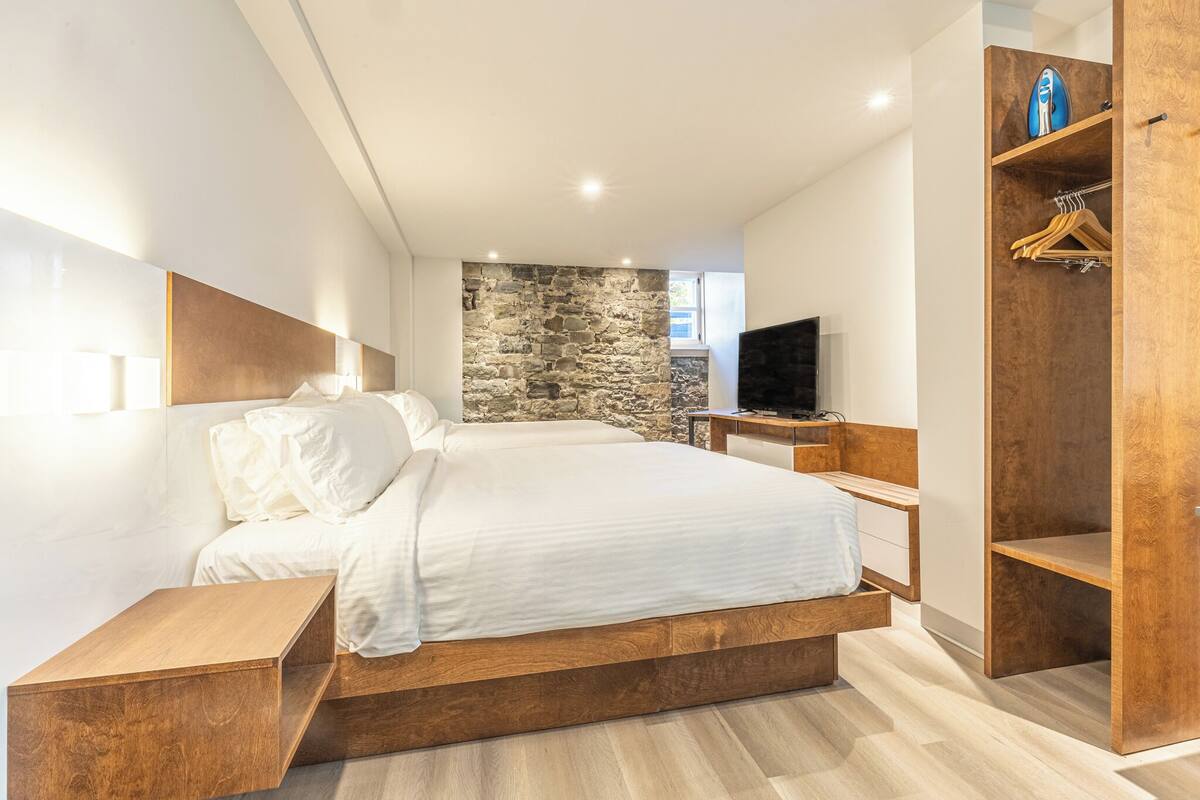 Ein modernes Schlafzimmer mit einem großen Bett, einer Wand aus Stein, einem Holzschrank und einem Fernseher.
