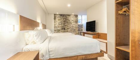 Un dormitorio moderno con una cama grande, un muro decorativo de piedra, un armario de madera y un televisor.
