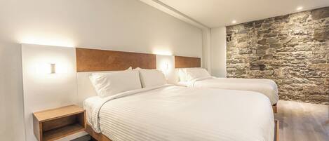 A modern bedroom with two beds, wooden headboards, a stone accent wall, and built-in nightstands.