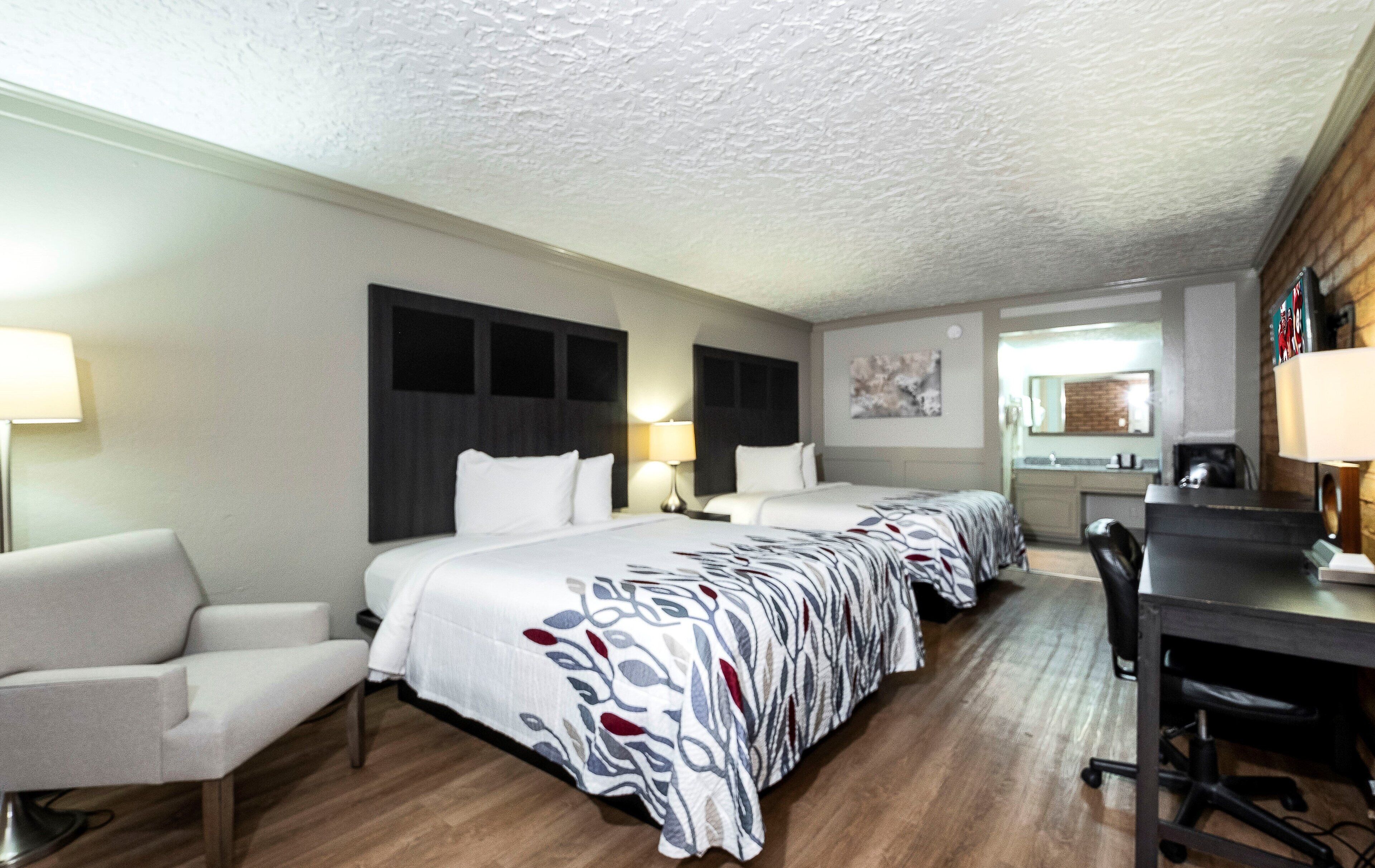 Een hotelkamer met een groot bed, een bureau, een stoel en een badkamer die door een geopende deur zichtbaar is.