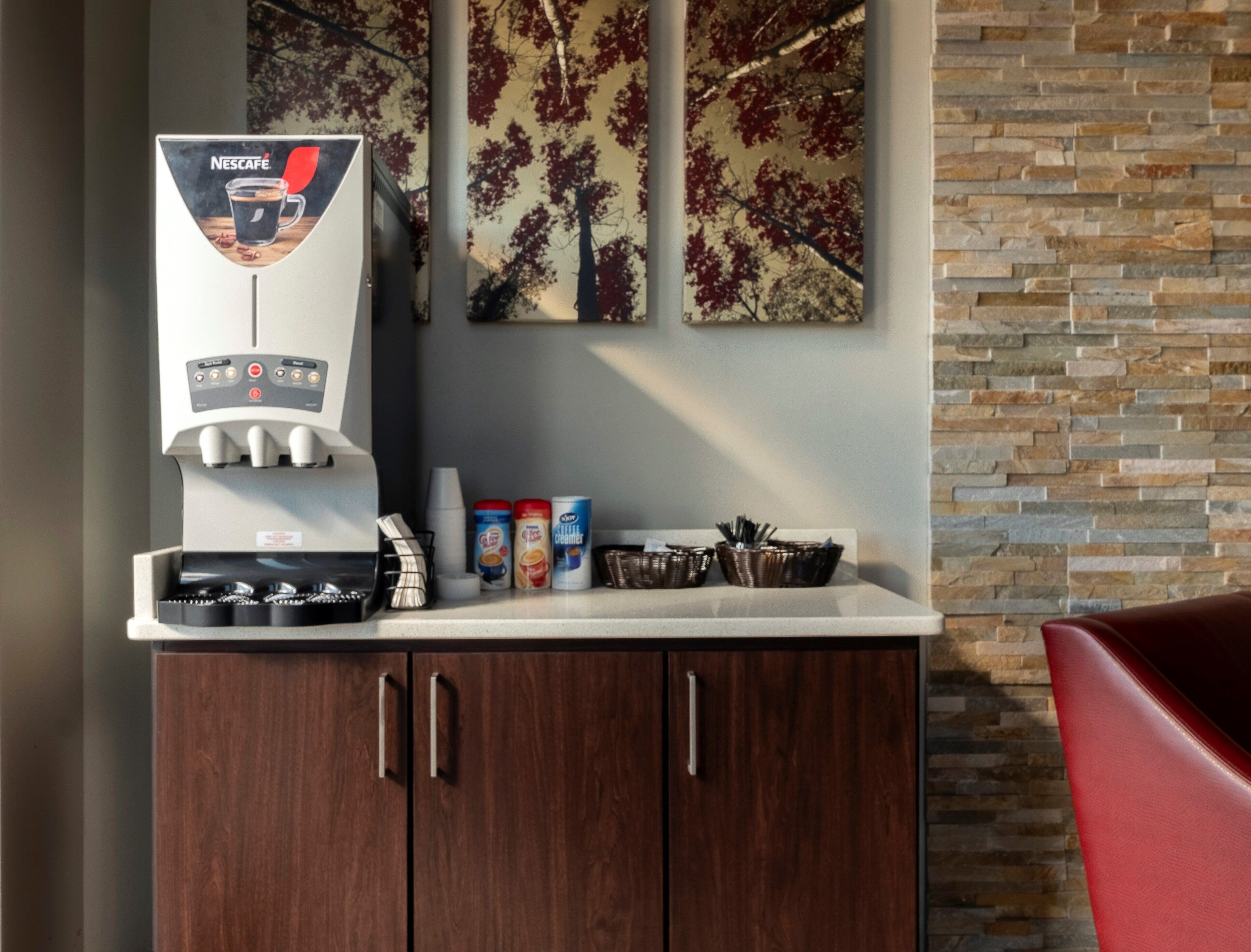Una cafetera con el logotipo de Nescafé, un mostrador con varios artículos y una pared con un diseño de árboles.