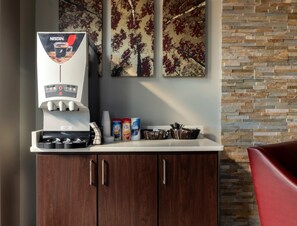 A coffee machine with a Nescafe logo, a counter with various items, and a wall with a tree pattern.
