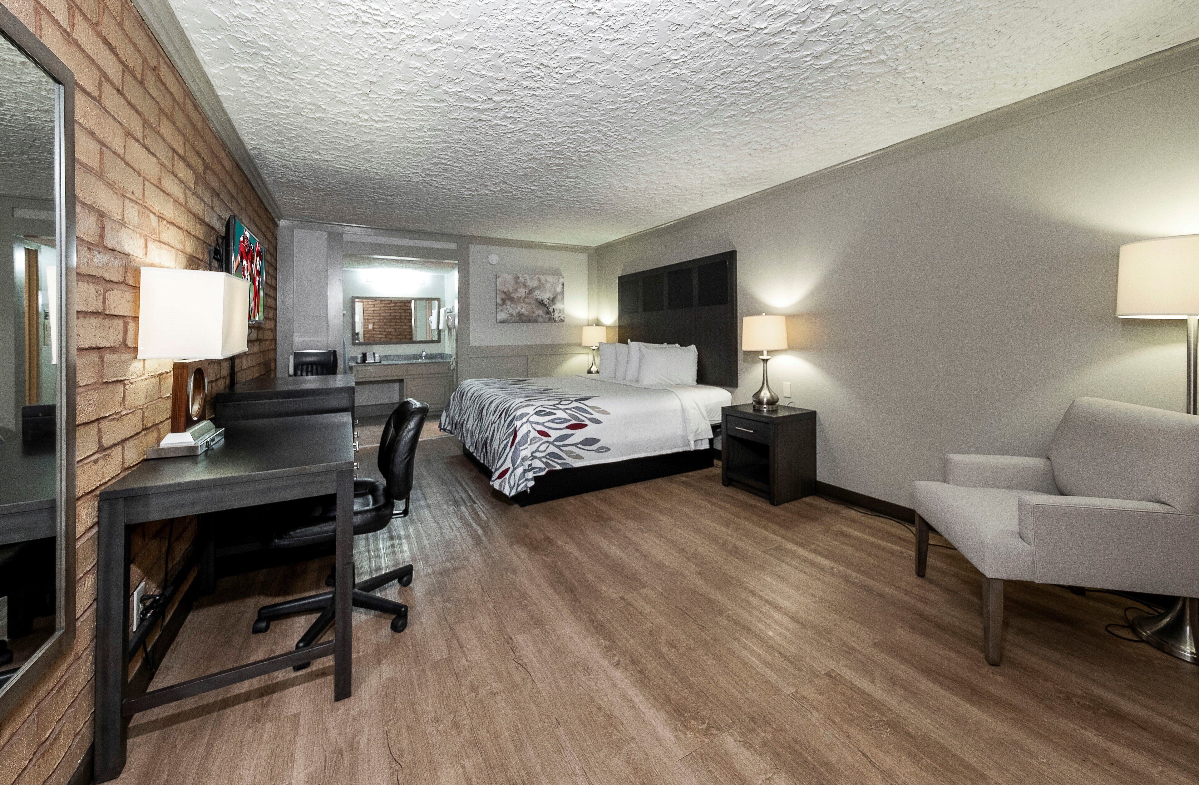 A hotel room with a bed, desk, chair, and a small table.