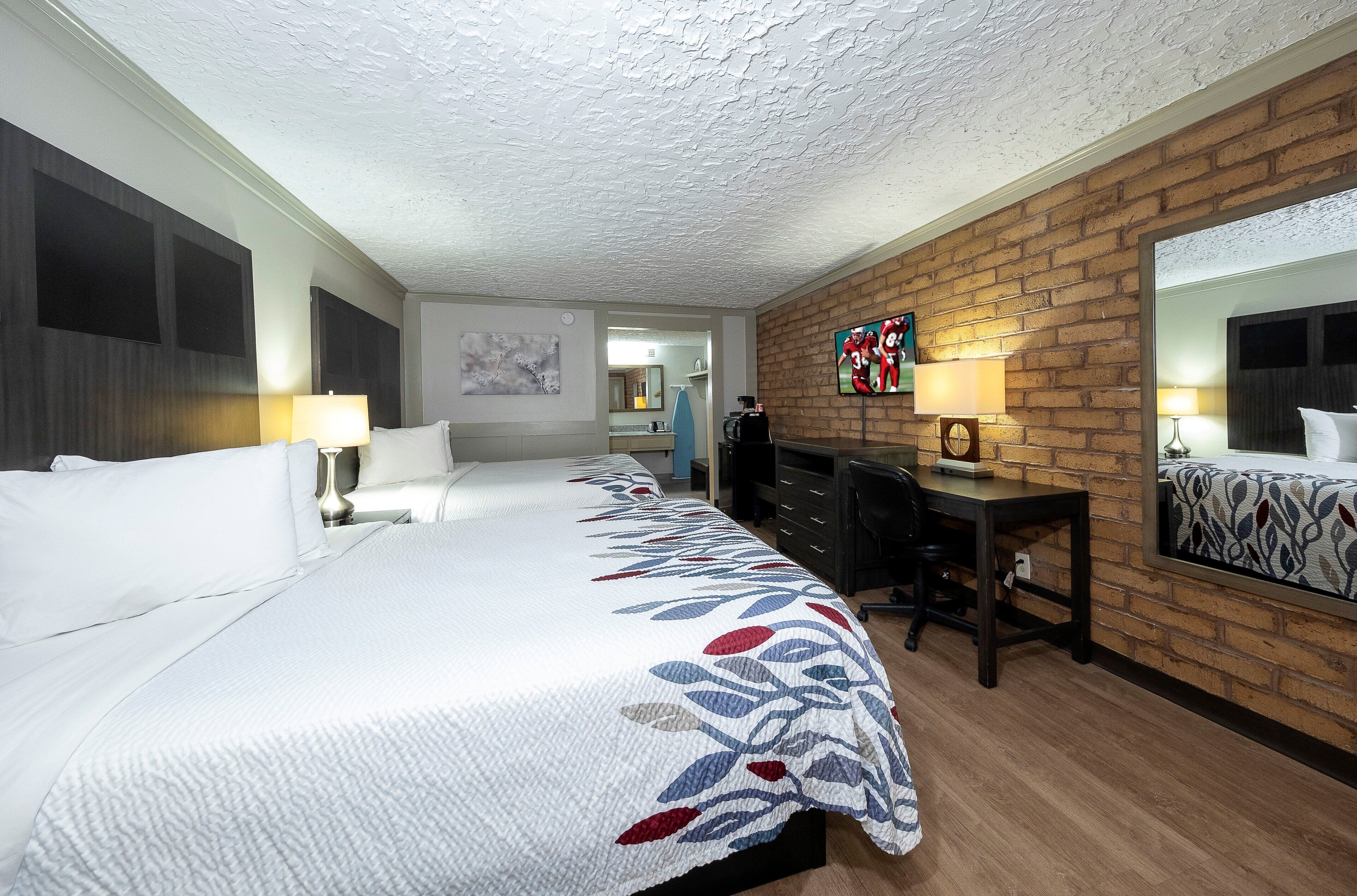 Een hotelkamer met een groot bed, een bureau, een spiegel en een televisie aan de baksteenwand.