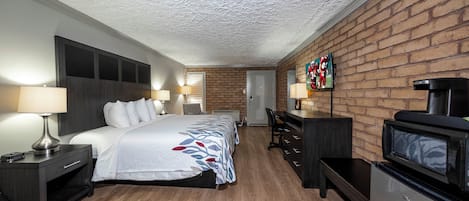 A hotel room with a bed, desk, TV, and a brick wall.