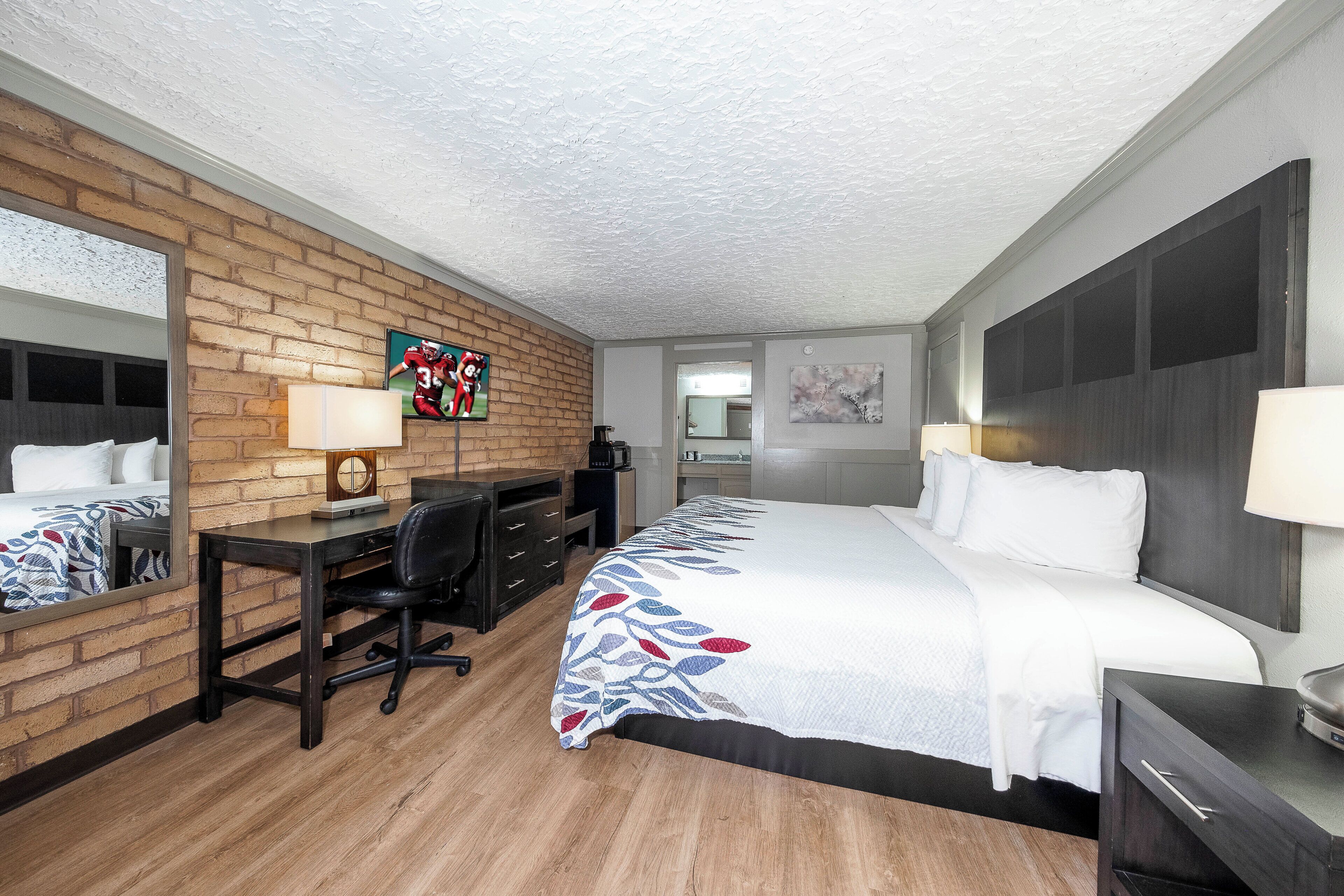 Habitación de hotel con pared de ladrillo decorativa, un escritorio con silla, cama con colcha estampada y un espejo grande.
