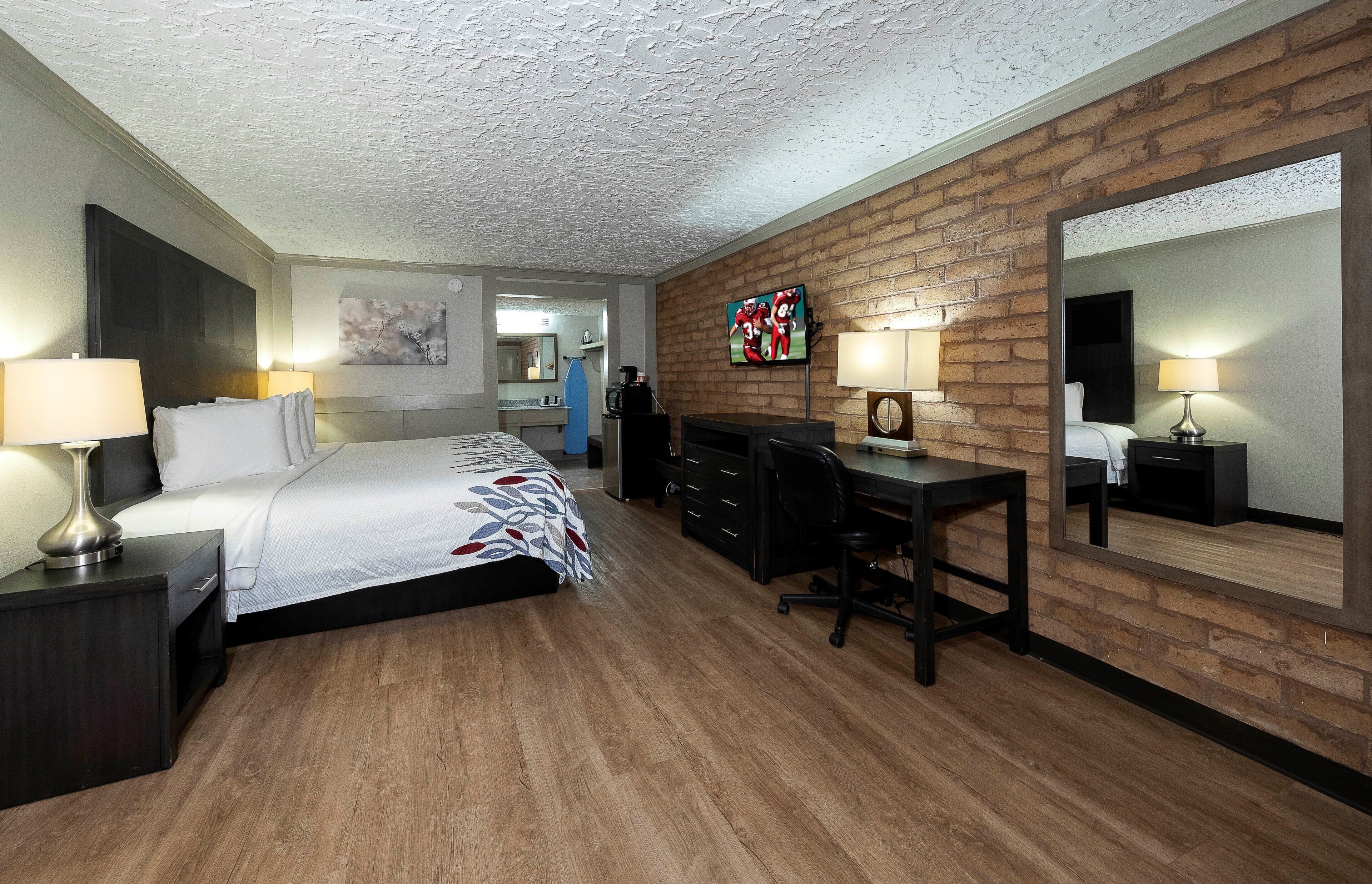 A hotel room with a bed, desk, chair, and a television.