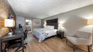 A hotel room with a bed, desk, chair, and a small kitchenette.