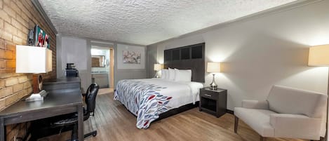 A hotel room with a bed, desk, chair, and a small kitchenette.