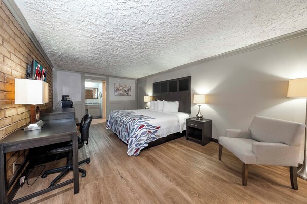 A hotel room with a bed, desk, chair, and a small kitchenette.