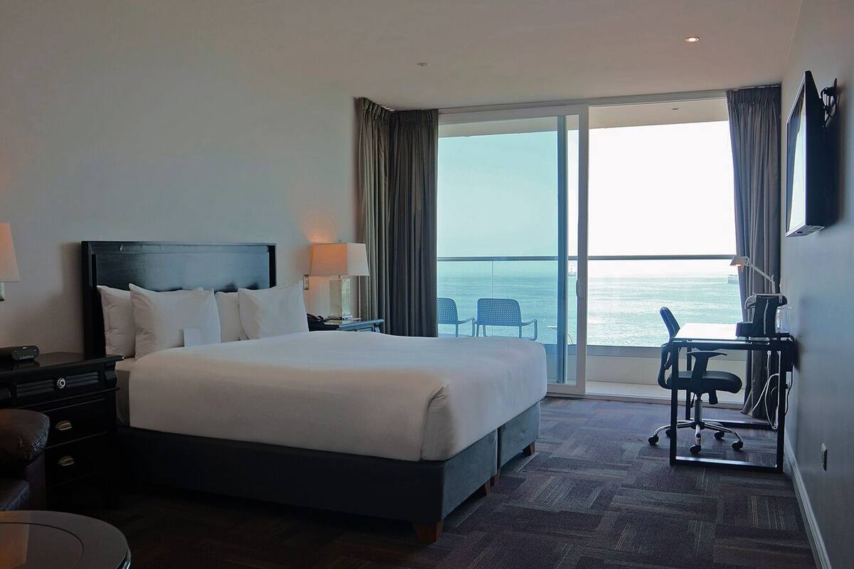 Une chambre d’hôtel avec un grand lit, un bureau, une chaise et une vue sur l’océan.