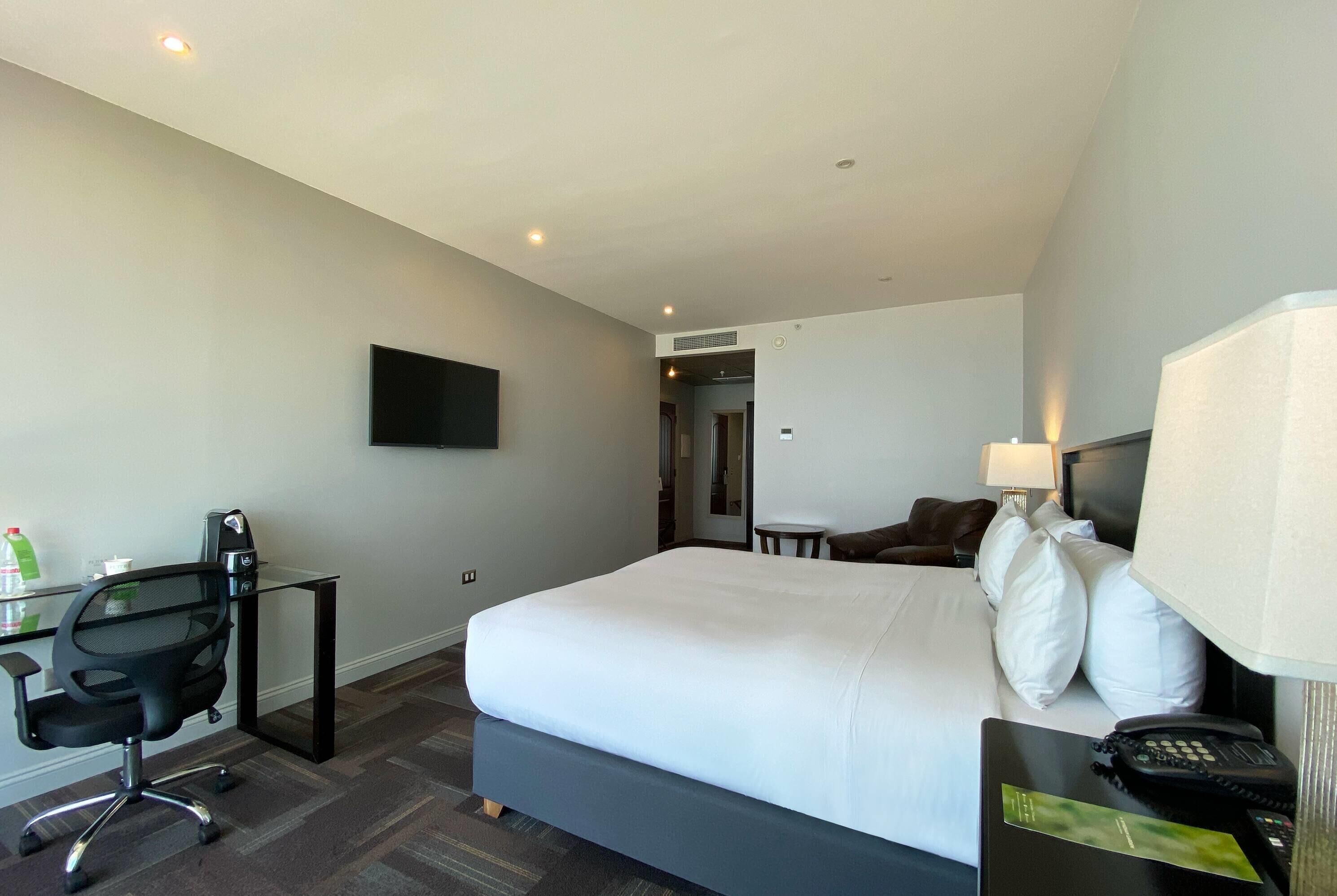 Habitación de hotel con una cama grande, un escritorio con silla, un televisor de pantalla plana, una lámpara y un teléfono.