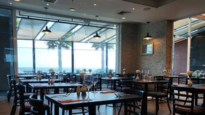 Un restaurante con varias mesas y sillas, amplios ventanales y luminarias colgantes.