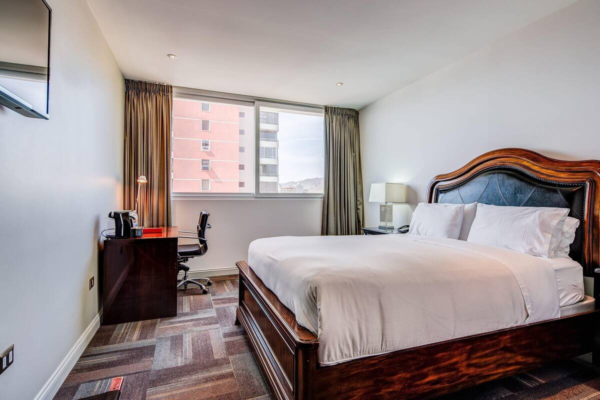 Une chambre d’hôtel avec un grand lit, un bureau, une chaise, une lampe et une fenêtre avec des rideaux.