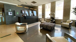 Un área de recepción moderna con un mostrador oscuro, zona de estar con sillas y grandes ventanales que dejan entrar luz natural.