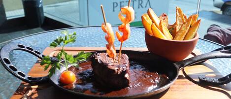 A meal with steak, fries, and shrimp on a plate, with a sign in the background reading "WYNDHAM GARDEN PETRA".