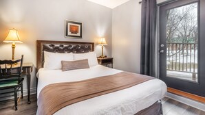 A hotel room with a large bed, two bedside lamps, a framed picture on the wall, and a view through the door. - Hôtel Jardin Du Gouverneur (Québec City)