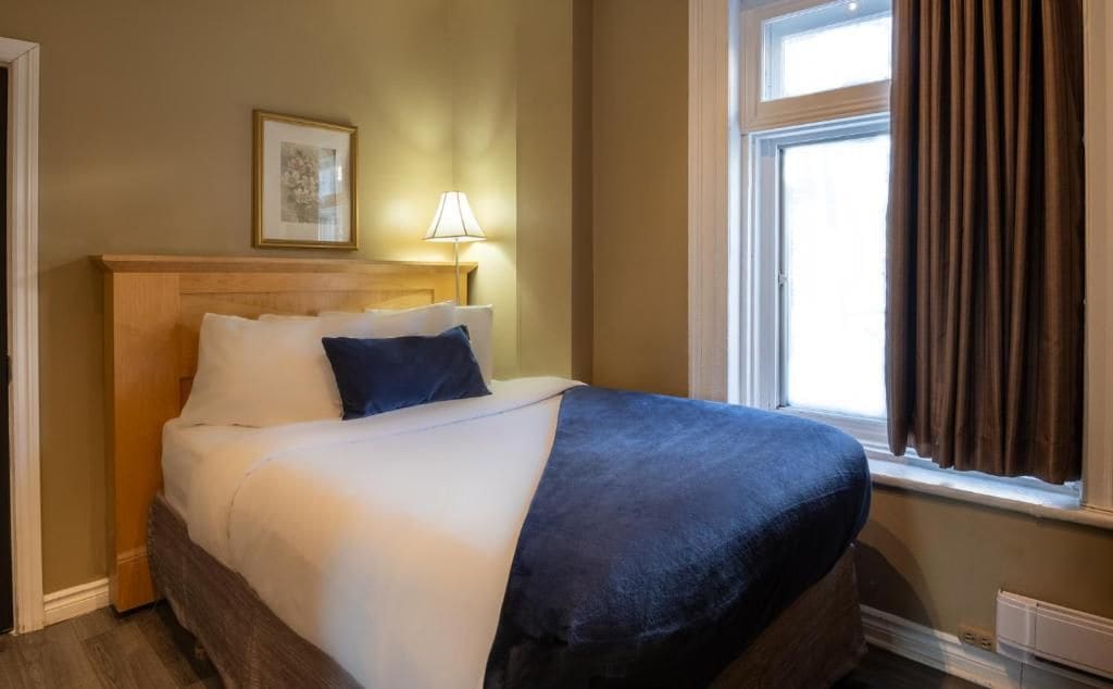Een hotelkamer met een bed, een bedlamp, een raam met gordijnen en een ingelijst schilderij aan de muur.