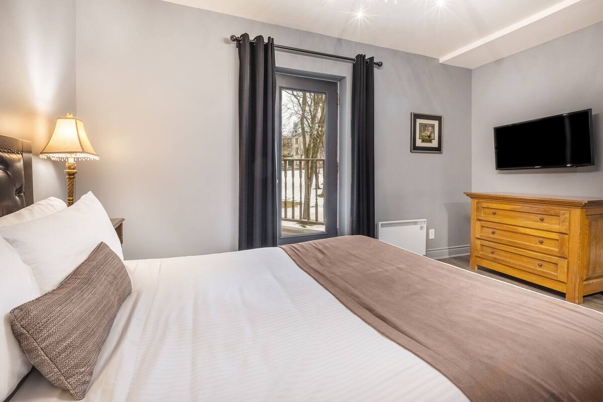 Een hotelkamer met een bed, een houten dressoir, een televisie en een raam met gordijnen.