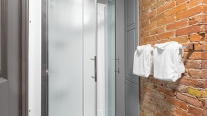 A bathroom with a glass shower door, a white bathtub, and a brick wall. - Hôtel Jardin Du Gouverneur (Québec City)