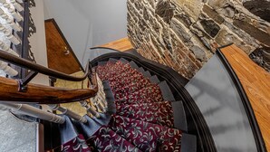 Una escalera de caracol con alfombra estampada, barandillas de madera y pared de piedra.