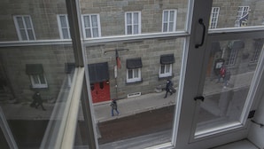 Vista a través de una ventana de un edificio de varios pisos con muros de piedra y múltiples ventanales.