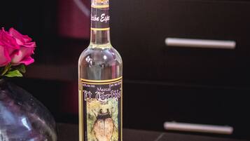 Una botella de Mezcal Toreno sobre una mesa con dos vasos para tequila y un florero con una flor rosa.