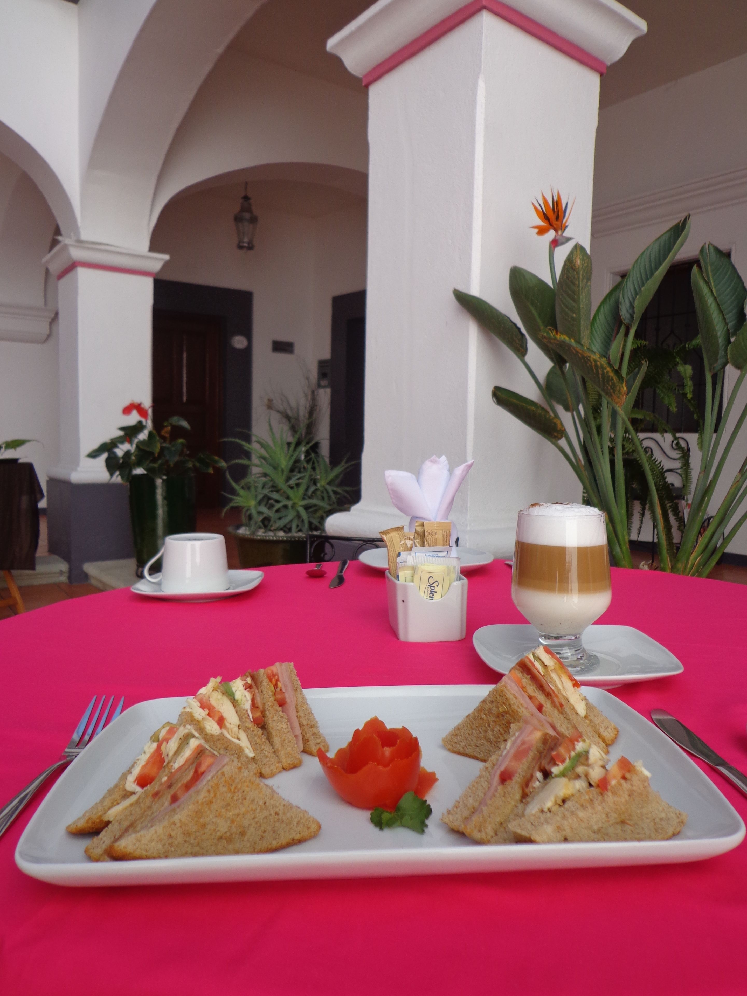 Una mesa preparada para una comida con sándwiches, una rosa y una bebida.