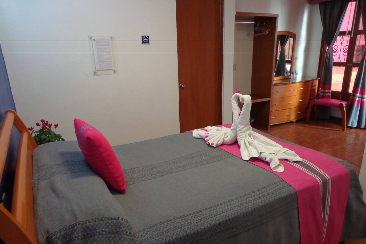 A hotel room with a bed, a wooden chair, a dresser, and a mirror.