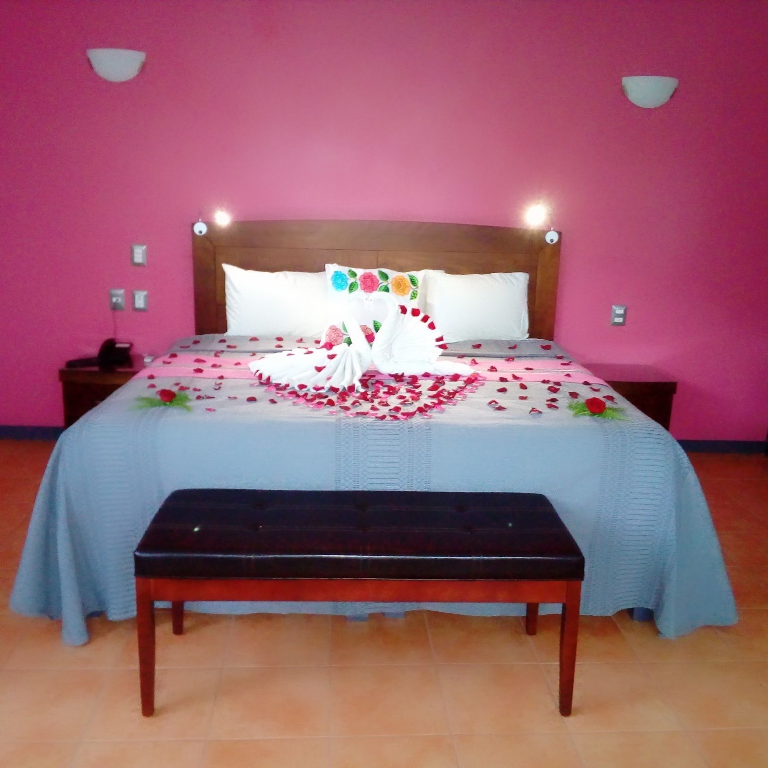 Una cama con una colcha blanca y rosa estampada con flores, un cabecero de madera y un banco al frente.