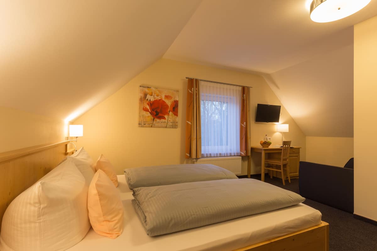 Una habitación de hotel con cama, escritorio, silla, televisor y ventana con cortinas.