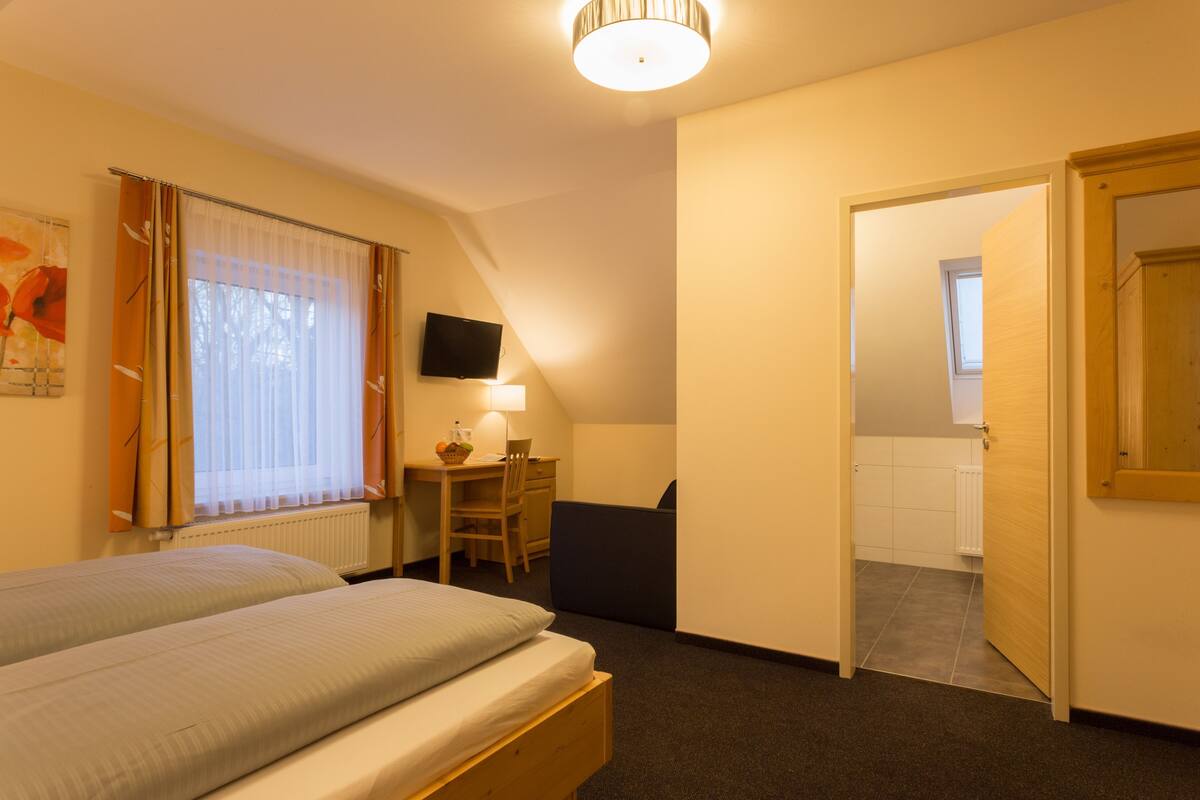 Habitación de hotel con cama, escritorio, silla, televisor y puerta que da a otra habitación.