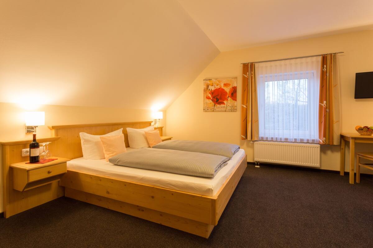 Un dormitorio con cama de madera, lámparas de noche, mesita de noche, ventana con cortinas y televisor montado en la pared.